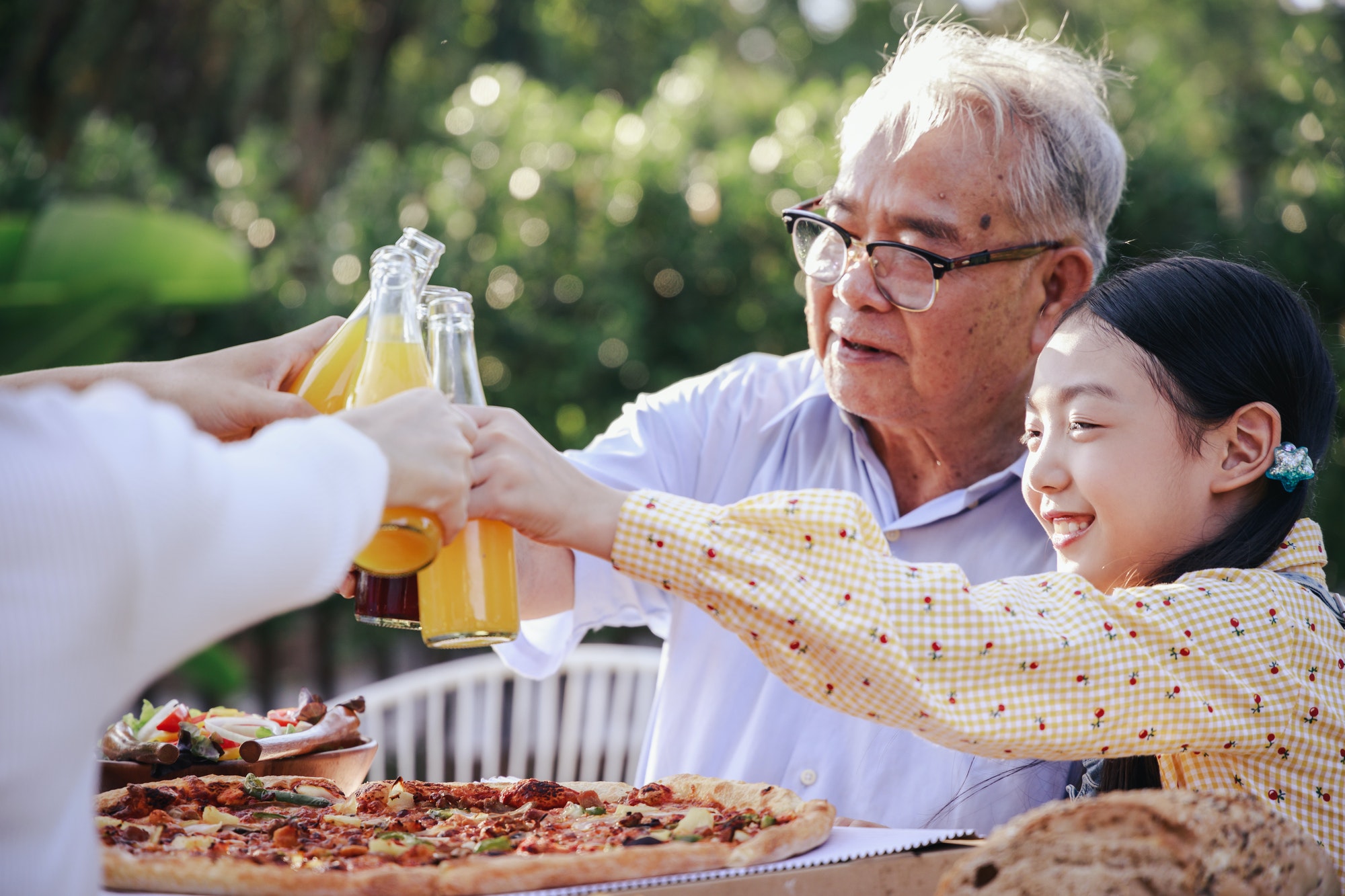 Happy Asian family having enjoying meal together and cheers of orange juice at home garden